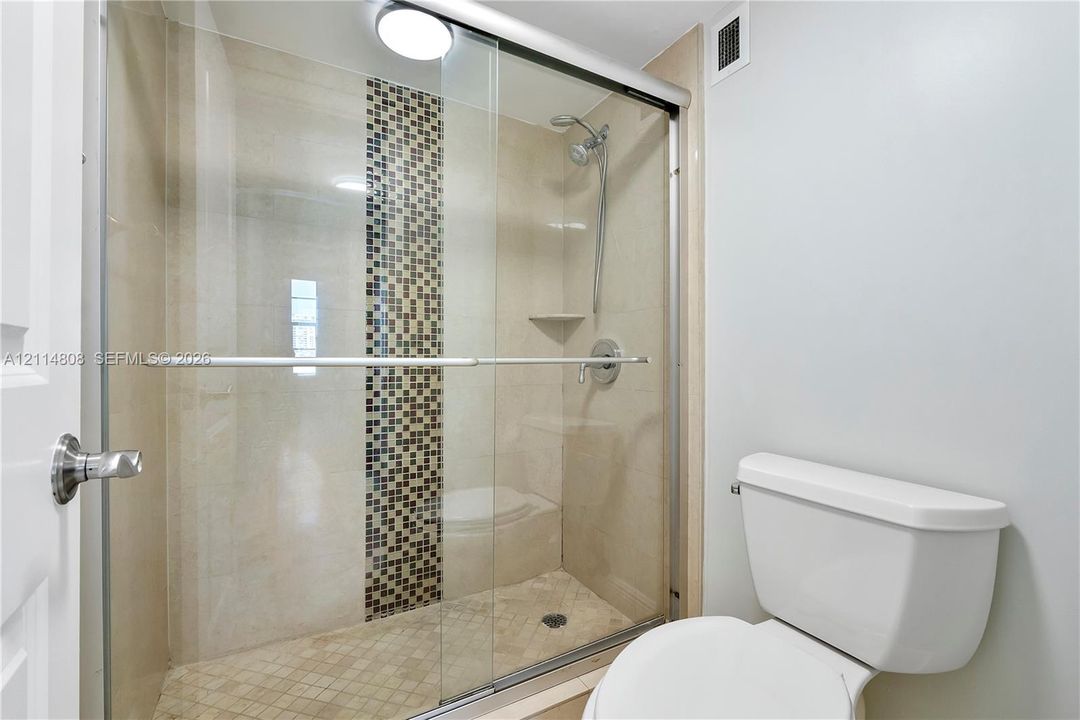 Walk-in shower featuring a sliding glass enclosure, decorative vertical tile accent, built-in corner shelving, integrated shower head with handheld attachment, and tile flooring