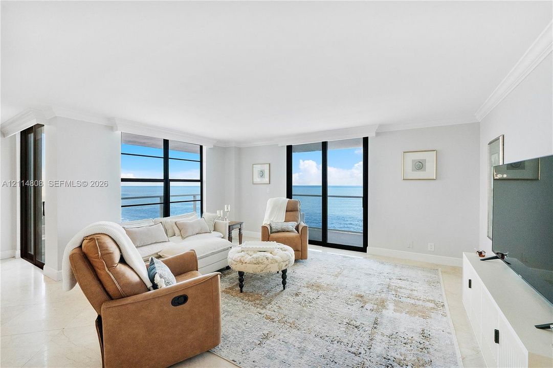 Living area featuring large-format tile flooring, crown molding, and floor-to-ceiling windows with direct ocean exposure