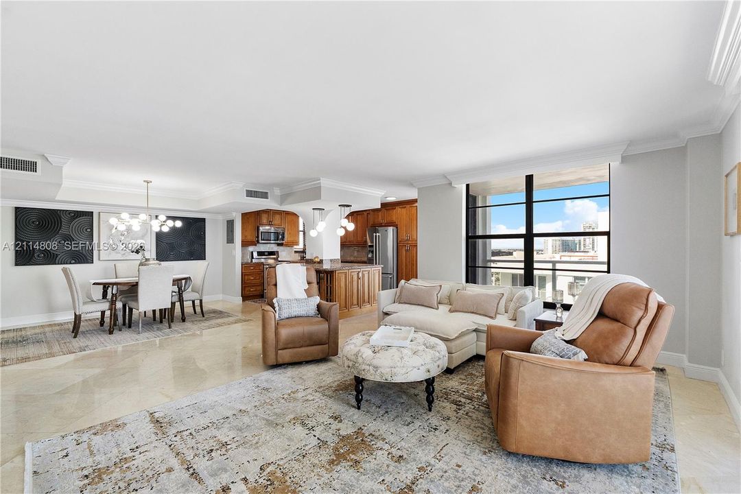 Open-concept living space featuring stone flooring, floor-to-ceiling windows, crown molding, built-in cabinetry, and integrated multi-pendant lighting