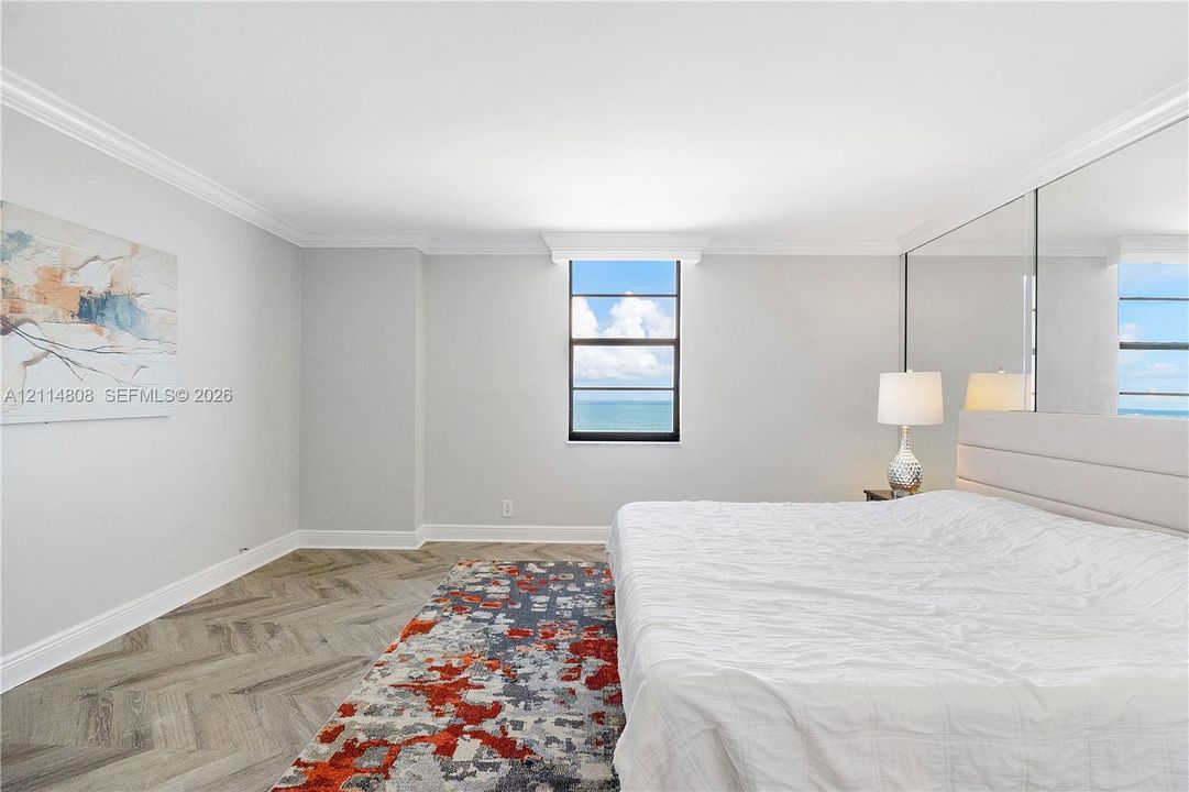 Herringbone wood-finish flooring, ceiling crown molding, floor-to-ceiling mirrored wall, and ocean horizon backdrop