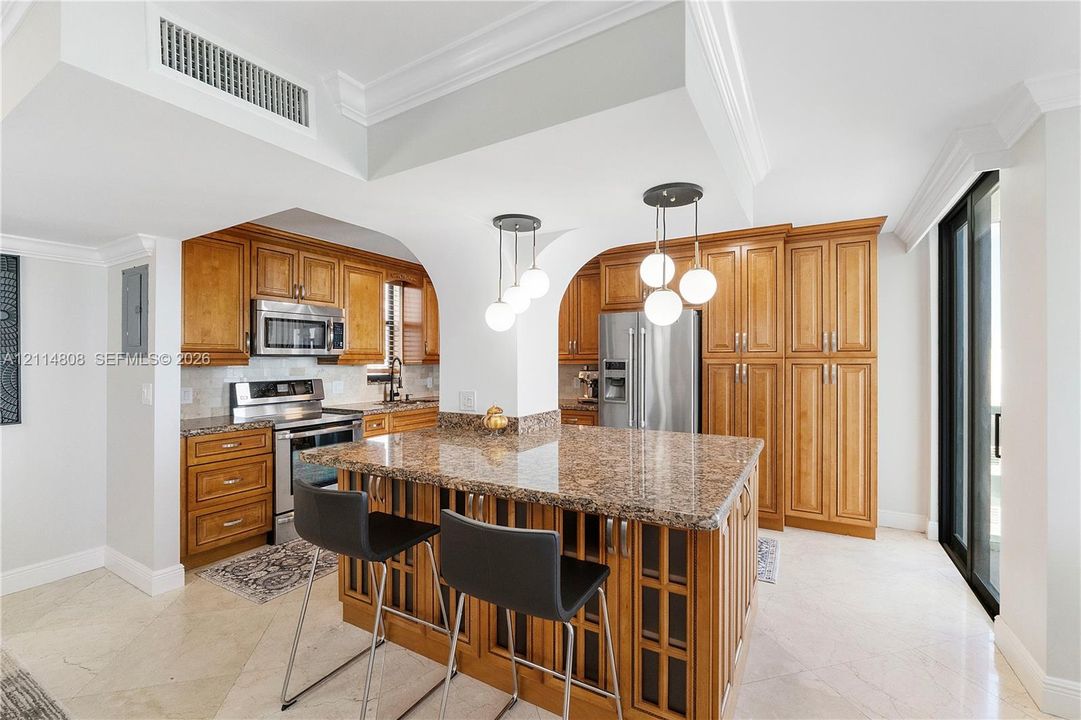 Kitchen featuring stone countertops, custom cabinetry, a center island, stainless steel appliances, and pendant lighting