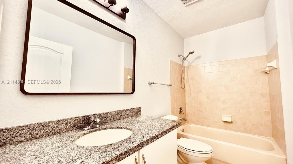 Bathroom featuring a stone-composite countertop, undermount sink, rectangular mirror with a dark frame, and a tub-shower combination with ceramic tile surround