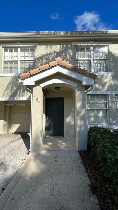 Two-story exterior featuring a covered entryway, tile-accented roof peak, grid-patterned windows, and an attached garage