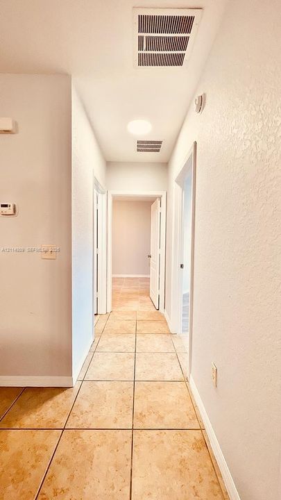 Interior hallway featuring large-format neutral tile flooring, smooth walls, and multiple door frames