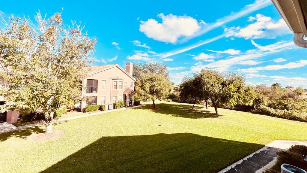 Expansive lawn area featuring mature shade trees, paved walkways, and building exterior with a stucco finish and chimney stack