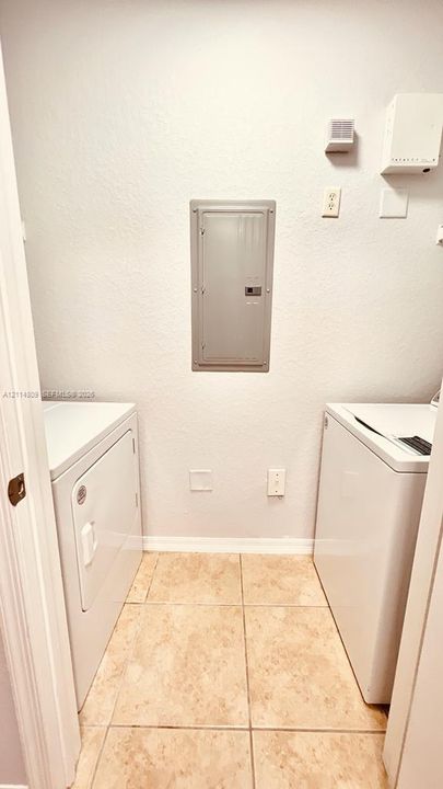 Utility space featuring large-format stone-finish floor tile, wall-mounted electrical service panel, and dedicated laundry appliance hookups