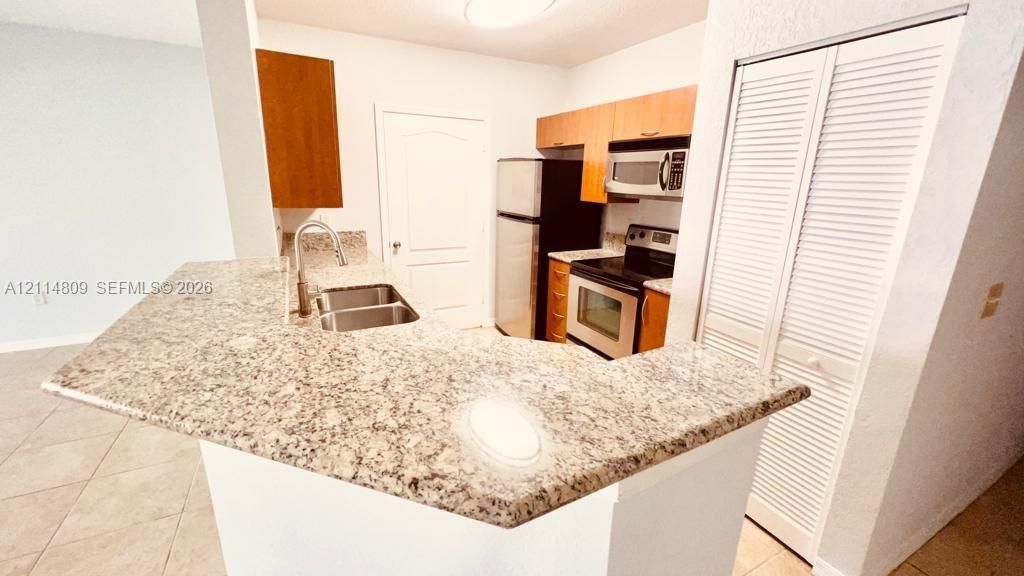 Kitchen featuring a stone-look breakfast bar with a dual-basin undermount sink, stainless steel appliances, wood-finish cabinetry, and tiled flooring