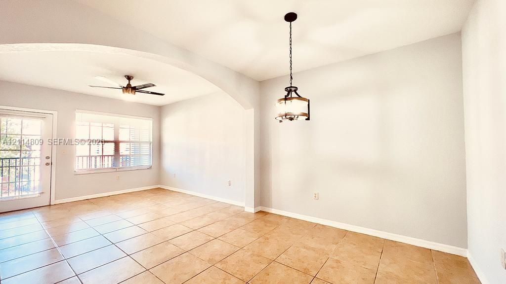 Open-concept interior featuring tile flooring, an arched architectural detail, a multi-pane glass door, a ceiling fan, and a decorative pendant light fixture