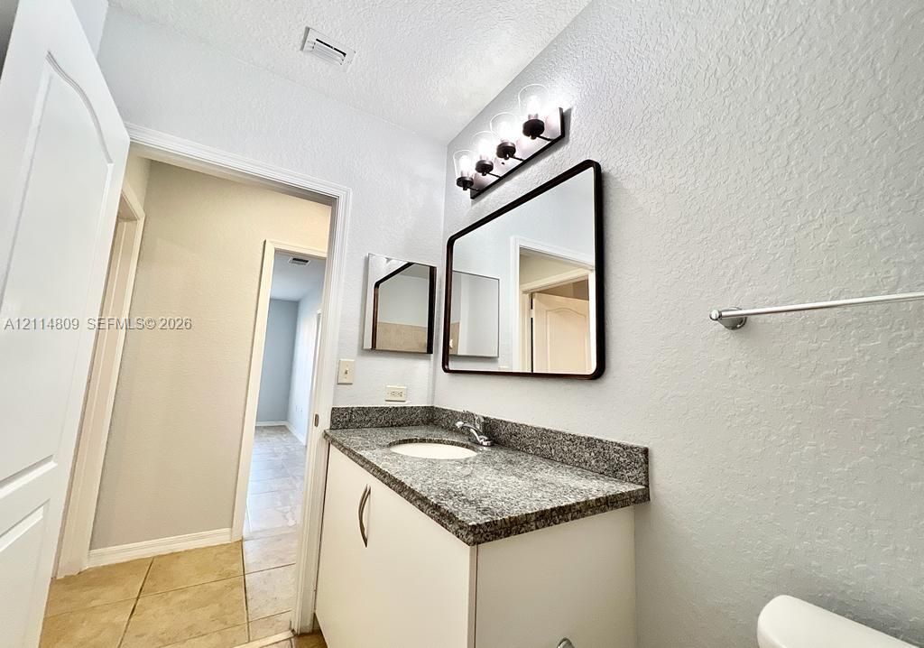 Vanity featuring a stone-composite countertop with an integrated basin, contemporary rectangular mirror with a dark frame, and multi-bulb fixture with glass shades
