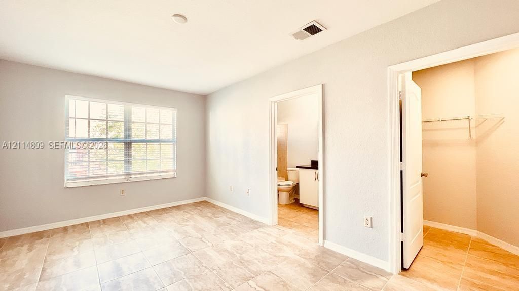 Neutral-toned room featuring large grid-pane windows, tile flooring, and a walk-in closet