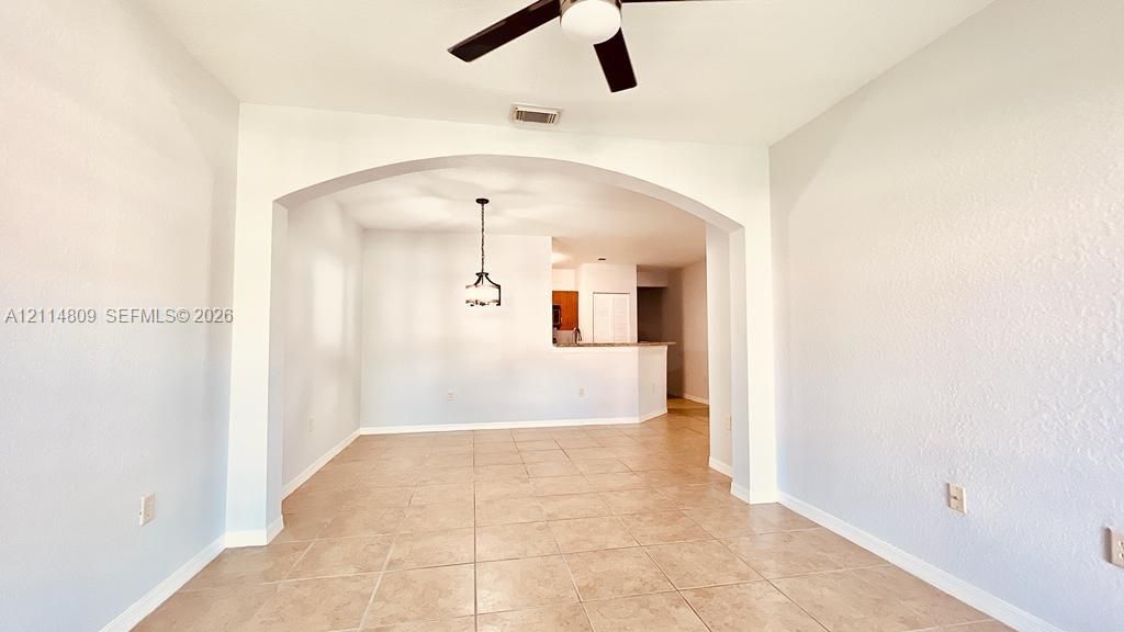 Interior space featuring ceramic tile flooring, a prominent architectural archway, and a ceiling fan with integrated lighting