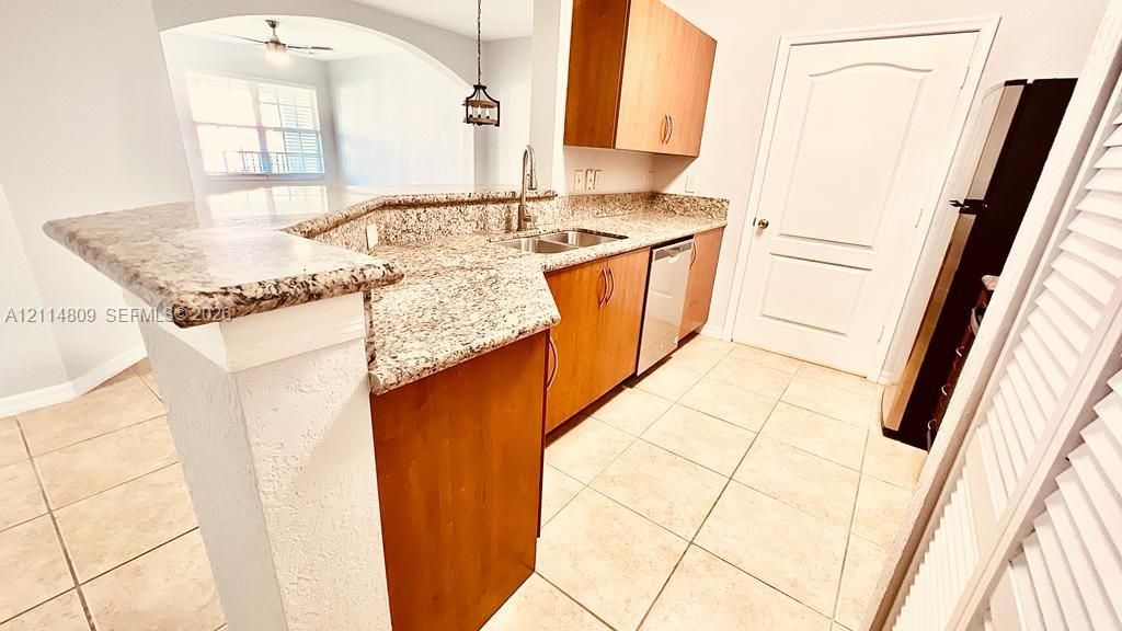 Kitchen featuring stone-patterned countertops, wood-finish cabinetry, stainless steel sink with high-arch faucet, and tile flooring