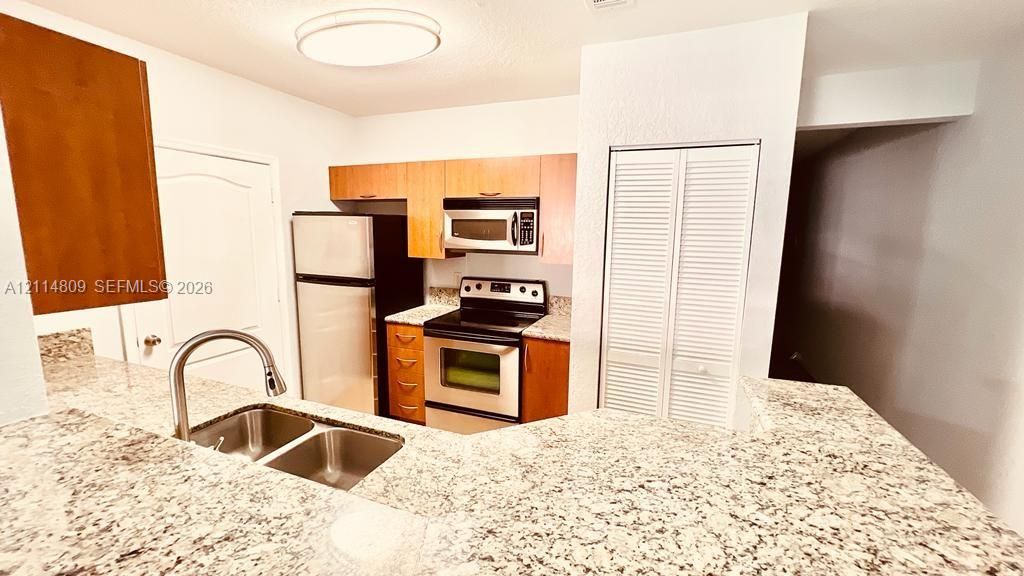 Kitchen featuring stone-finish countertops, stainless steel appliances, flat-panel cabinetry, a dual-basin undermount sink with a gooseneck faucet, and a louvered closet door