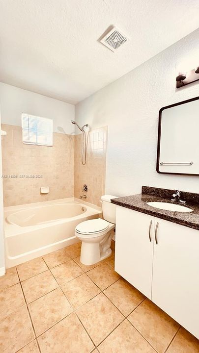 Bathroom featuring a soaking tub with tile surround, vanity with dark stone-finish countertop, undermount sink, and rectangular wall-mounted mirror