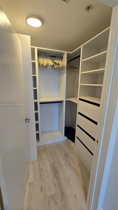 Walk-in closet featuring white built-in shelving, integrated dresser drawers, dual hanging rods, and wood-finish flooring