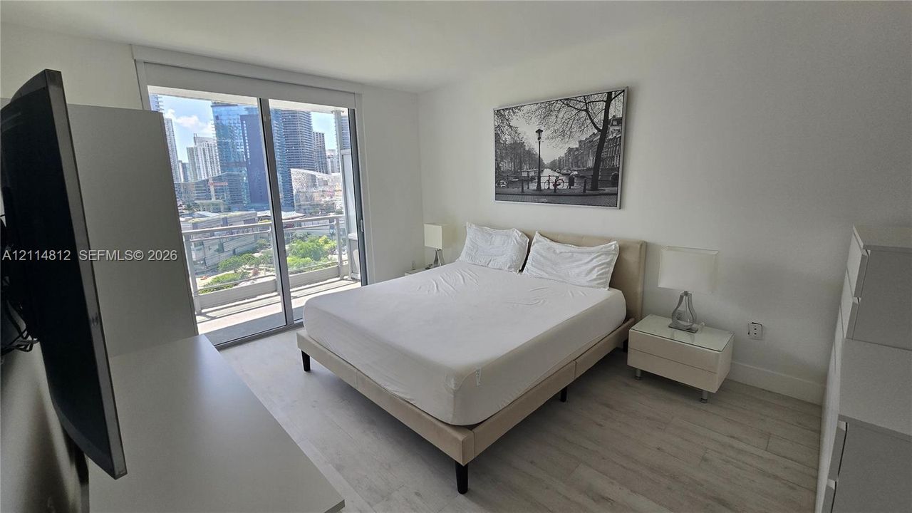 Sliding glass doors opening to a private balcony with cityscape scenery, complemented by light-toned wood-finish flooring