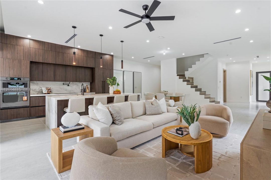 Modern kitchen featuring flat-panel wood cabinetry, stone-finish waterfall edge island, built-in double wall ovens, recessed lighting, and a contemporary ceiling fan