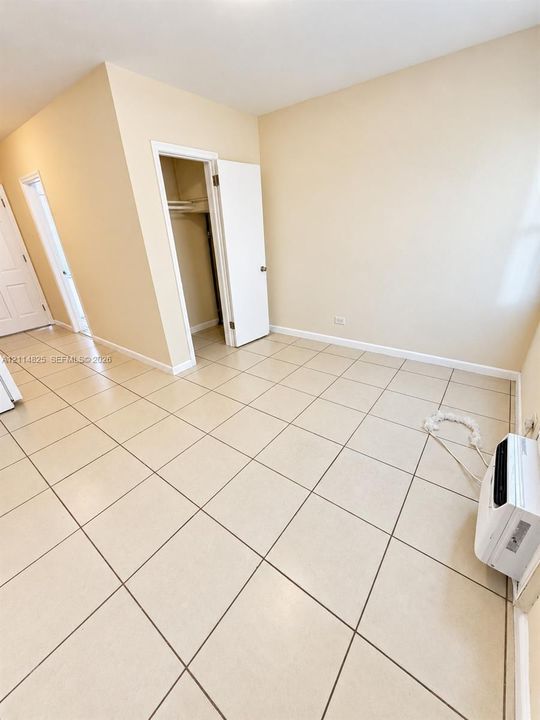 Neutral-toned interior featuring ceramic tile flooring, a dedicated closet with built-in shelving, and a wall-mounted cooling unit
