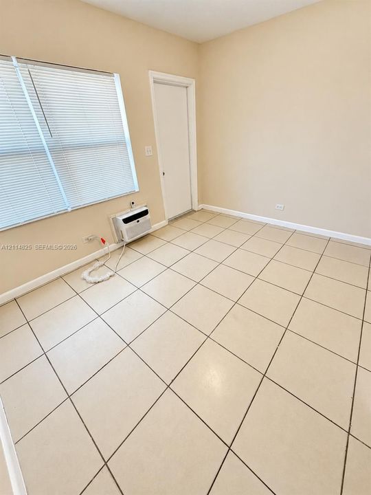 Room featuring neutral wall paint, large-format tile flooring, a window with horizontal blinds, and an integrated through-wall air conditioning unit