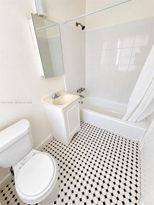 Bathroom featuring a black and white geometric tile floor, white tile tub surround, white vanity, wall-mounted medicine cabinet, and standard porcelain fixtures