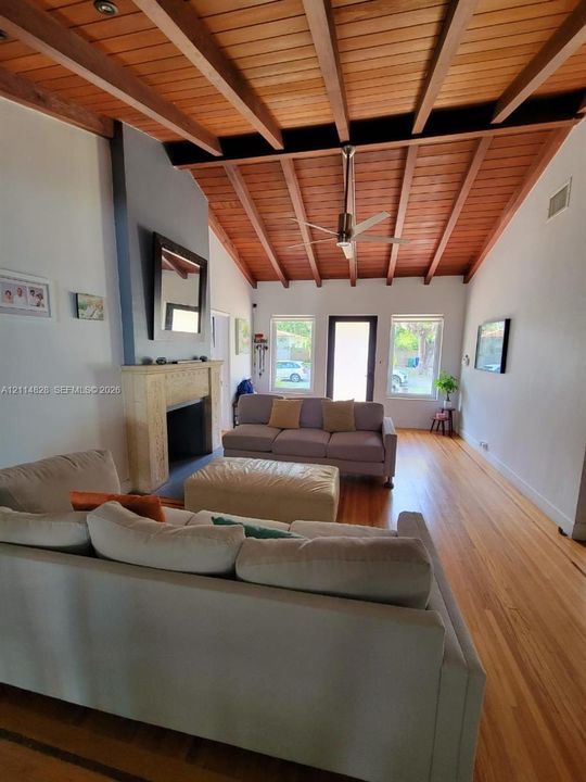 Vaulted wood-plank ceiling with exposed beams, wood-finish flooring, and stone-surround fireplace
