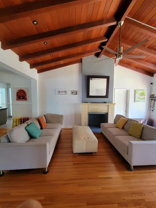 Vaulted wood-plank ceiling with exposed beams, wood-finish flooring, and stone-surround fireplace with built-in mantel