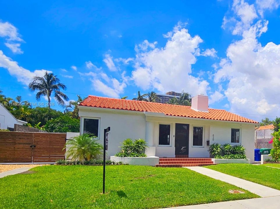 Spanish-style exterior featuring a terracotta tile roof, white stucco facade, brick entryway steps, and a horizontal wood-slat privacy gate