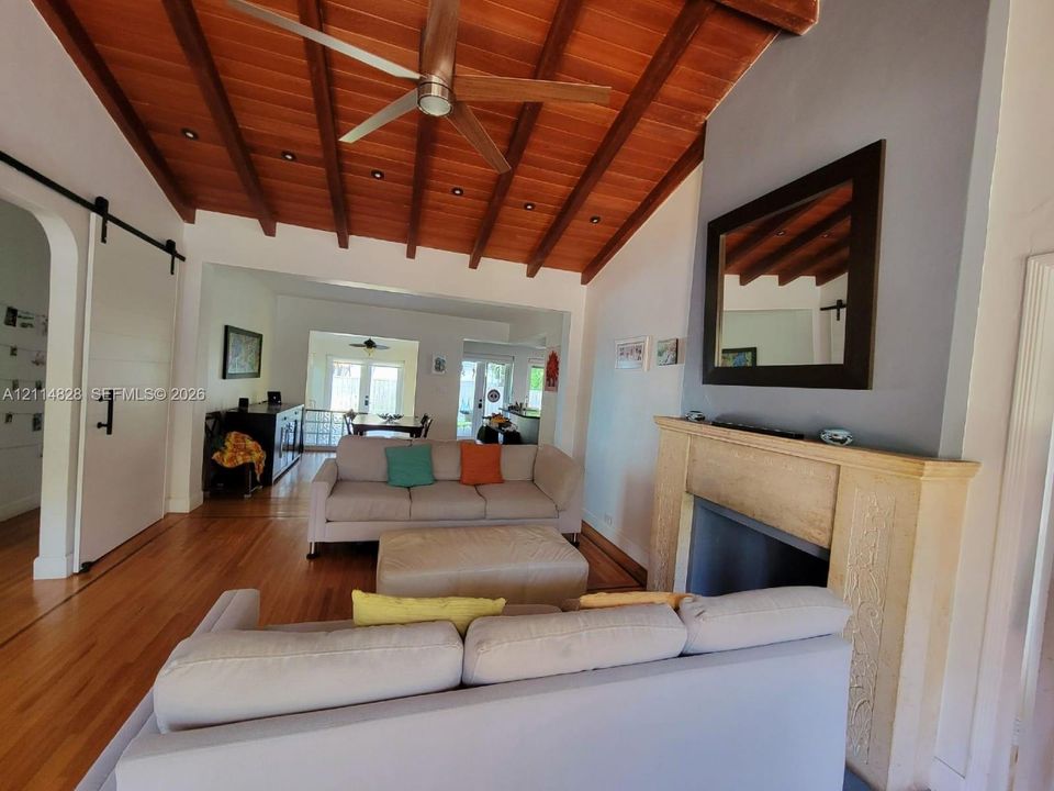 Vaulted ceiling with exposed wood beams, wood-finish flooring, stone-textured fireplace surround, and sliding barn door hardware