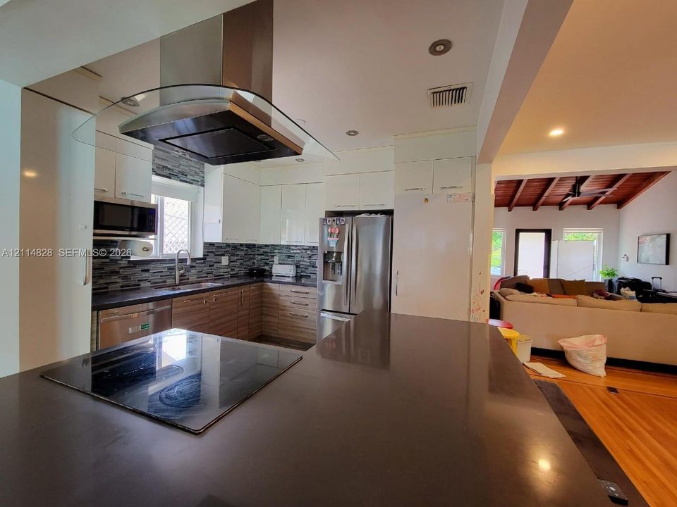Kitchen featuring white upper cabinetry, wood-finish lower cabinetry, stone countertops, stainless steel appliances, and a wall-mounted stainless steel vent hood