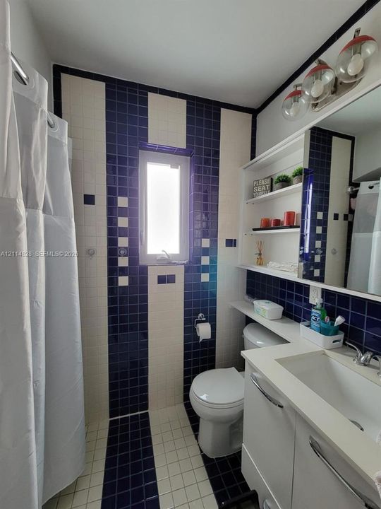Bathroom featuring a custom navy and white tiled wet room, integrated vanity with a solid-surface countertop, built-in open shelving, and multi-bulb wall-mounted lighting