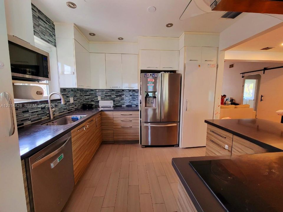 Kitchen featuring dual-tone cabinetry, dark solid-surface countertops, mosaic tile backsplash, stainless steel appliances, and wood-finish flooring