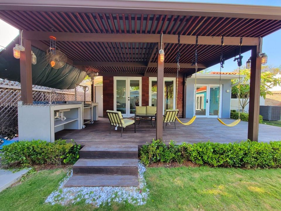 Covered patio featuring a wood-slat pergola, built-in outdoor kitchen with a stone-finish counter, recessed lighting, and wooden deck flooring