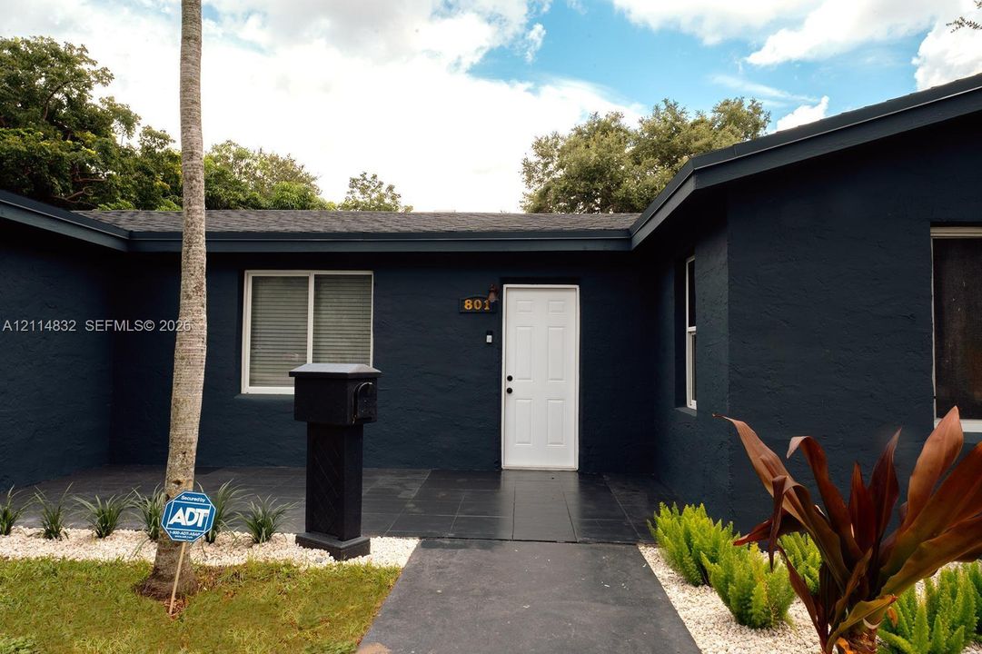 Single-story exterior featuring dark-toned stucco siding, tiled entryway, white-paneled entry door, and light-colored gravel landscaping beds