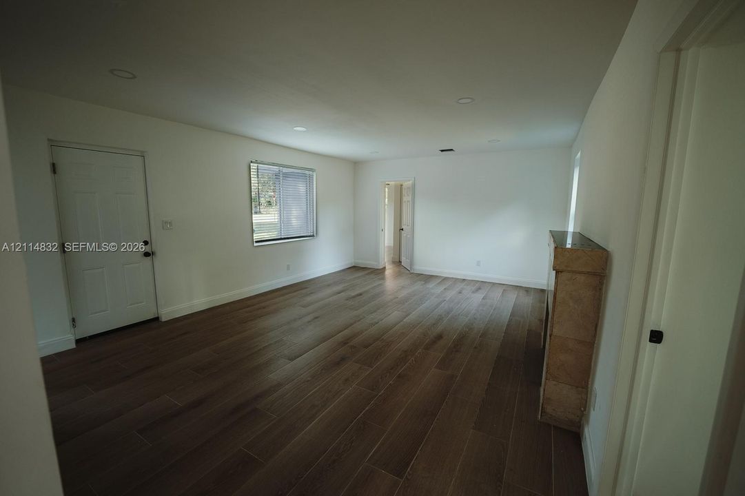 Open-concept interior featuring wood-finish flooring, recessed lighting, a stone-surround fireplace, and white paneled doors