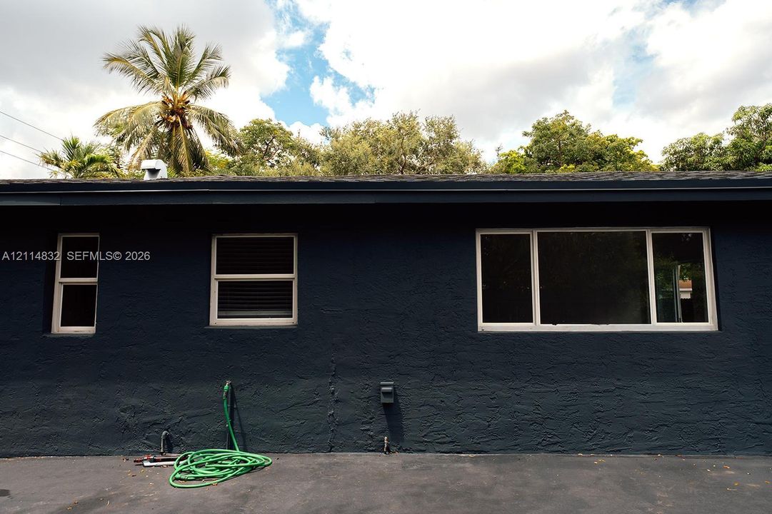 Textured dark exterior wall with multiple white-framed window units and asphalt surface