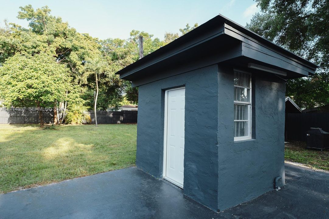 Detached structure featuring a dark-painted textured exterior, overhanging eaves, a single-entry door, a multi-pane window, and a paved foundation