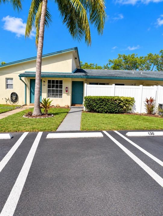 Exterior facade featuring a single-story design, dual entry doors, private white vinyl fencing, concrete walkways, and designated asphalt parking