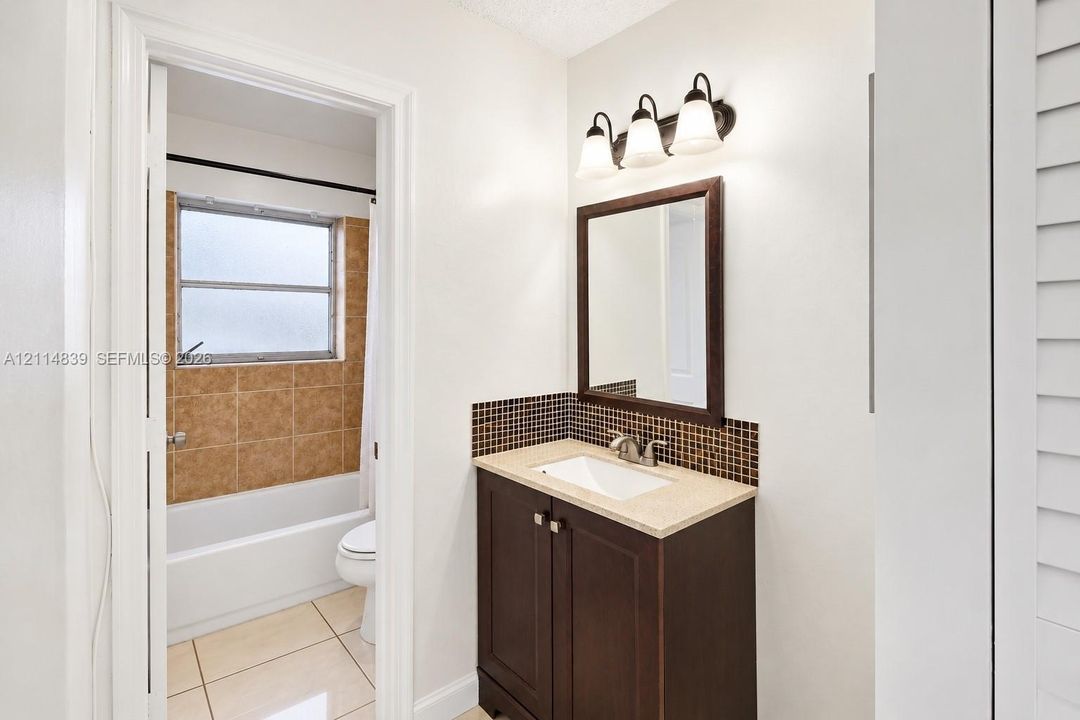 Bathroom featuring a dark wood-finish vanity with an integrated basin, stone-composite countertop, mosaic tile backsplash, and a three-light wall-mounted fixture