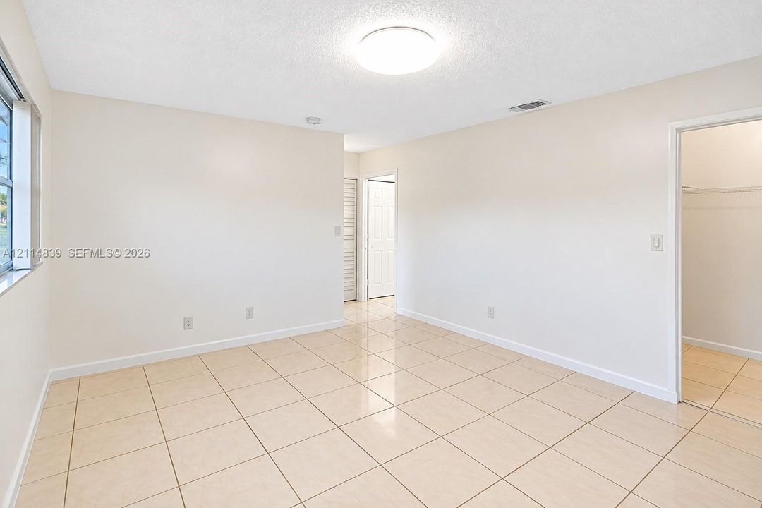 Neutral interior featuring large-format tile flooring, textured ceiling, flush-mount lighting, and a walk-in closet