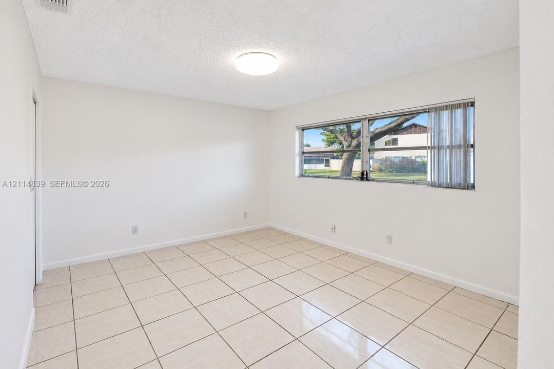Neutral interior space featuring polished tile flooring, light-toned walls, a flush-mount ceiling light, and a large window with horizontal blinds