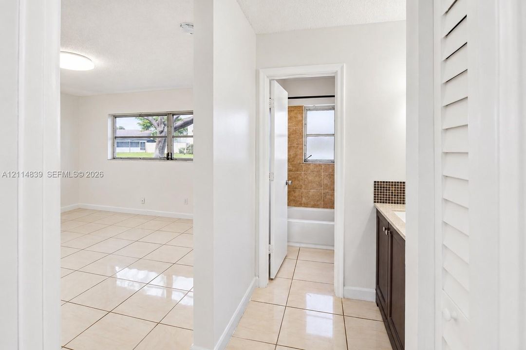 Large-format tile flooring, vanity with a stone countertop, square mosaic tile backsplash, louvered closet door, and tub-shower combination with textured wall tiling