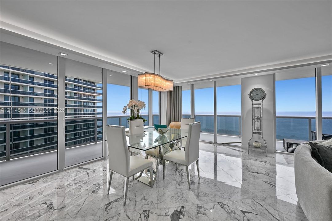 Floor-to-ceiling glass walls, polished stone flooring, recessed ceiling lighting, and a multi-light pendant fixture