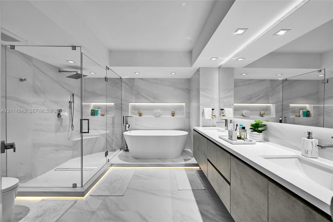 Bathroom featuring a glass-enclosed walk-in shower, freestanding soaking tub, dual-sink vanity with stone countertop, recessed wall shelving, and large-format tile flooring