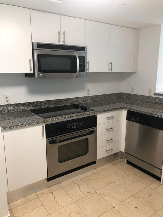 Kitchen featuring white flat-panel cabinetry, stone countertops, stainless steel appliances, and tile flooring