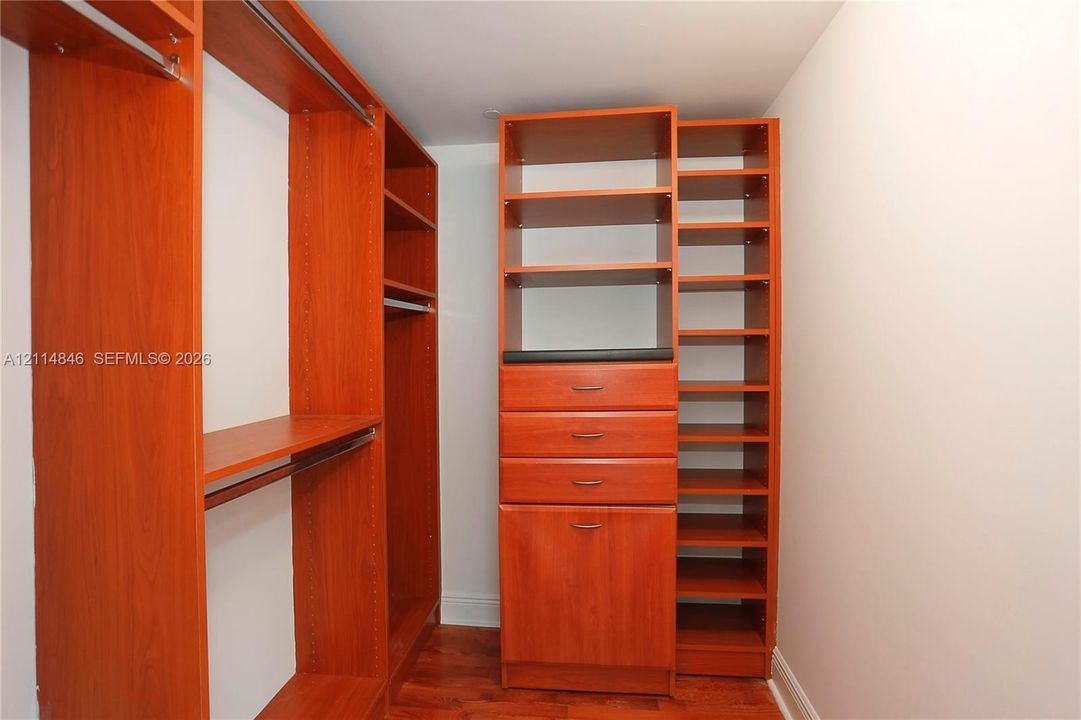 Custom closet featuring wood-finish cabinetry, integrated shelving, multiple storage drawers with metal hardware, and wood-finish flooring