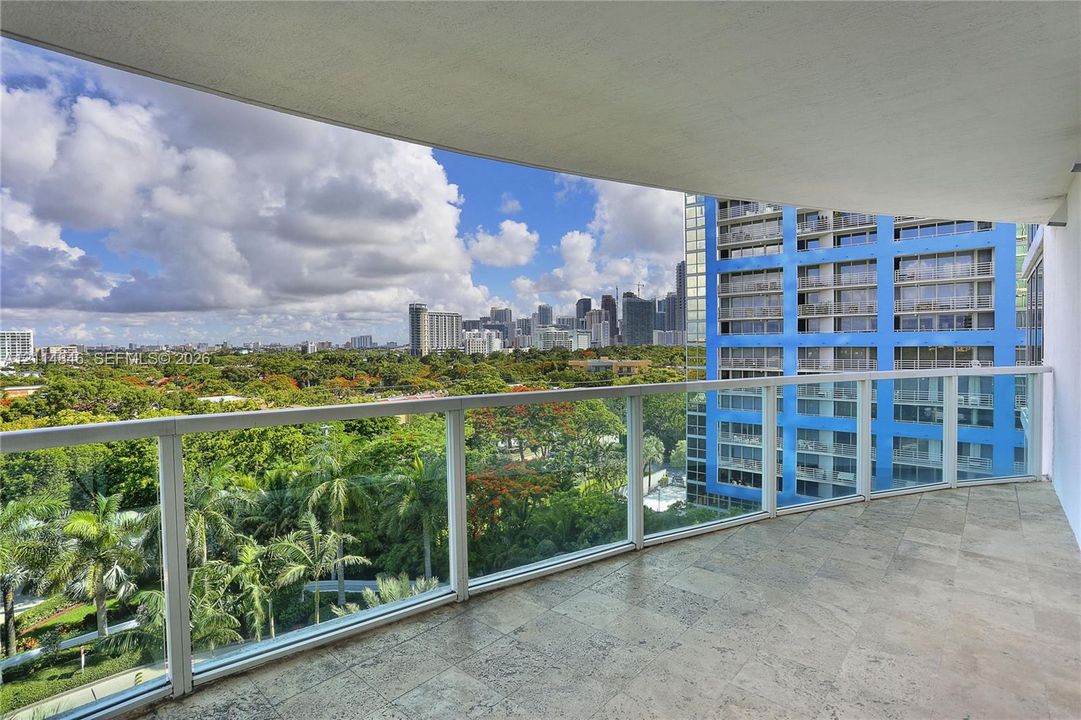 Covered balcony featuring stone tile flooring and a glass railing