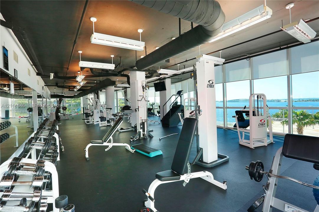 Fitness center featuring floor-to-ceiling windows, industrial-style exposed ceiling, rubberized flooring, and expansive water exposure