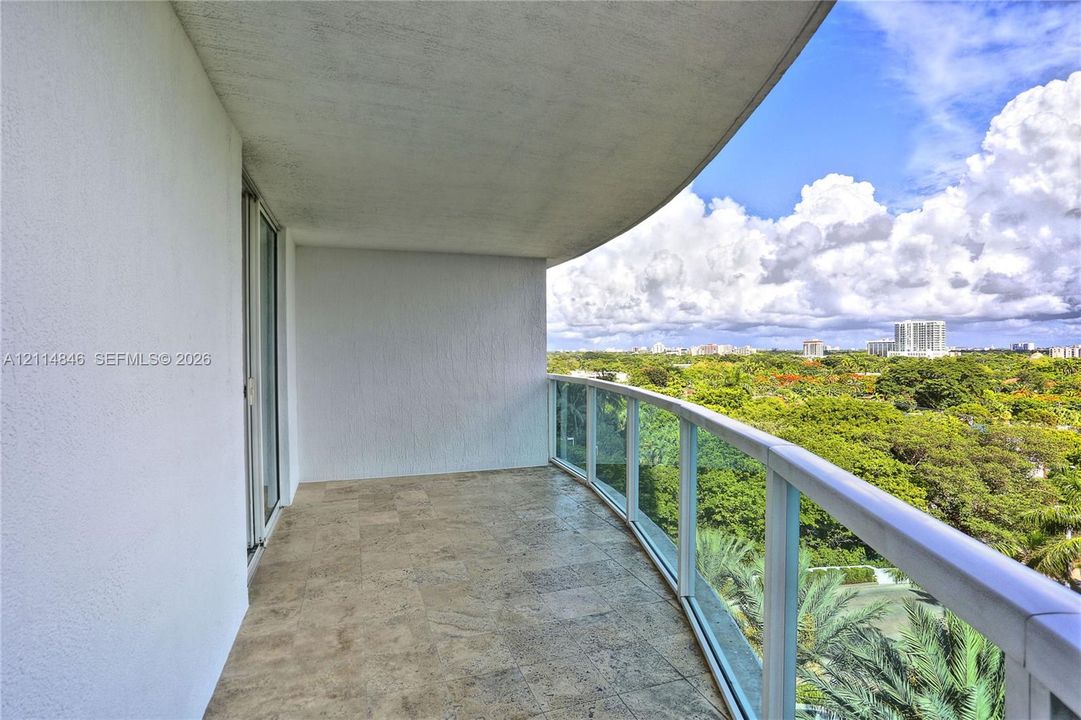 Covered balcony featuring stone-finish flooring, a curved concrete ceiling, and a glass-paneled railing