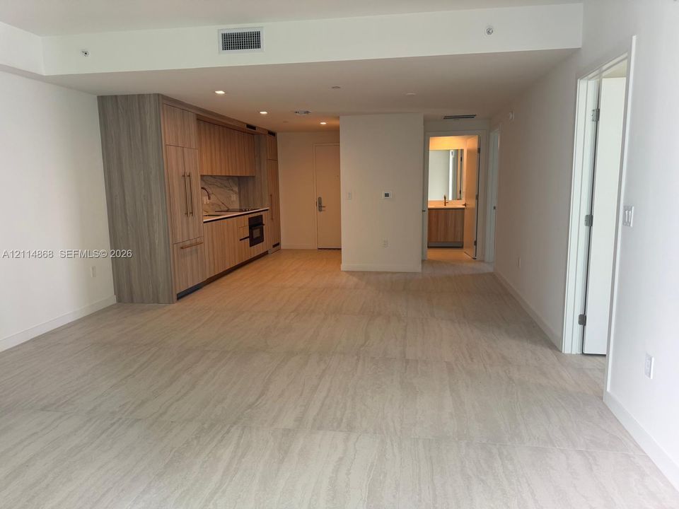 Open-plan living area featuring wood-finish cabinetry, stone-patterned backsplash, recessed lighting, and tile flooring