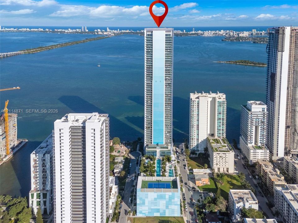 High-rise tower featuring multiple balconies, a ground-level swimming pool, and a rooftop sports court